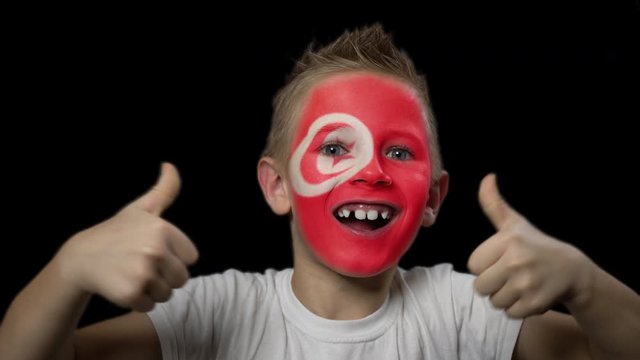 Happy boy rejoices victory of his favorite team of Tunisia. A child with a face painted in national colors. Portrait of a happy young fan. Joyful emotions and gestures. Victory. Triumph.