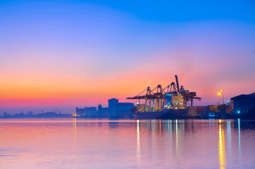 Fototapeta na wymiar View of container cargo ship and crane bridge in shipyard at sunrise