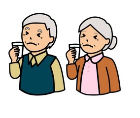 コップに入れた牛乳を飲んでしかめっ面をしている高齢者