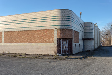 Long abandoned large brick retail building with rounded corners and weed covered sidewalks