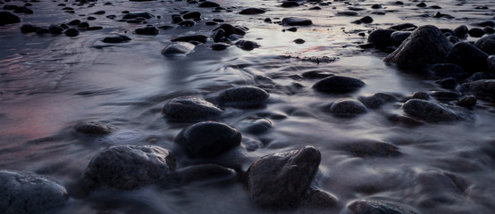 Water washes over pebbles along the coast in a long exposure shot of the tauranga harbour