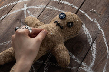 Voodoo doll on a wooden background with dramatic lighting. The concept of witchcraft and black art and the occult. Burlap doll on the background of a drawn star. Hand sticking pins into a doll.