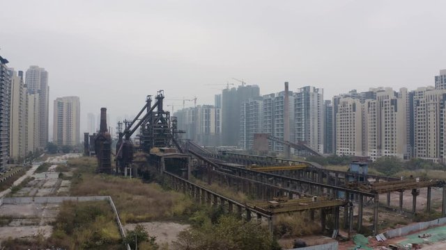 Abandoned steel mill factory with blast furnaces structures in between newly built apartment blocks on a cloudy day in Guangzhou, China, Aerial shot.