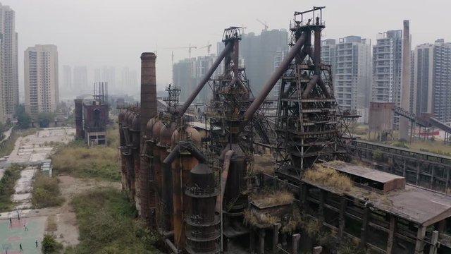 Slow fly by over abandoned steel plant metal structures in between living apartment blocks, Guangzhou, China, Aerial shot.