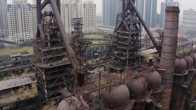 Slow rise up over abandoned steel plant metal structures with blast furnaces in between living apartment blocks, Guangzhou, China, Aerial shot.