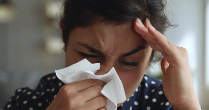 Allergic ill indian woman holding handkerchief blowing running nose