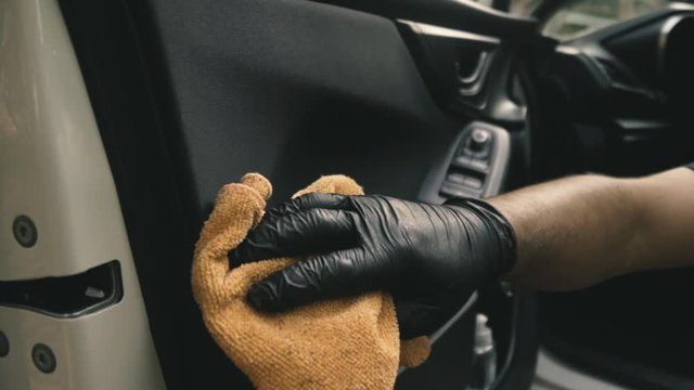 Close up of a male wearing black gloves cleaning a white car with black interior with a microfiber cloth in slow motion