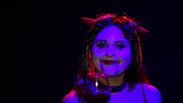 Woman devil with an ominous smile with a glass in his hand from blur to sharpness