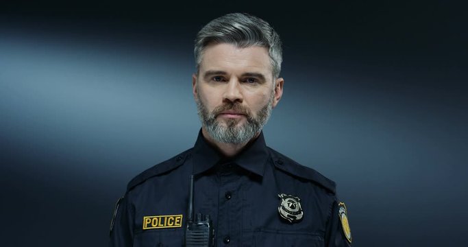 Portrait shot of the good looking Caucasian policeman with serious face and in the uniform looking straight to the camera. Close up.