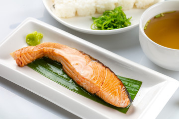 Grilled salmon with soy sauce with Japanese rice topped with black sesame seeds in a white plate on a white table