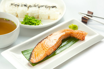 Grilled salmon with soy sauce with Japanese rice topped with black sesame seeds in a white plate on a white table
