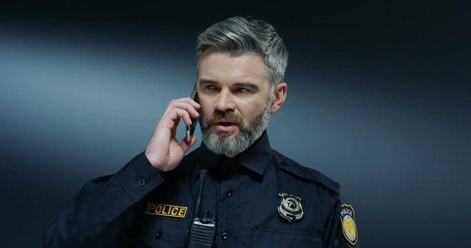 Caucasian handsome grey-haired policeman speaking on the mobile phone and deciding some important decisions.