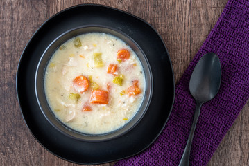 Greek lemon rice soup in a black bowl and black plate, black spoon and purple napkin, rustic wood table