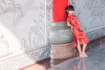 Asian child girl smiling in red dress standing on cement wall background, Concept costume Chinese new year