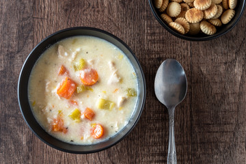 Greek lemon rice soup in a black bowl on a rustic wood table, spoon, oyster crackers