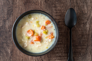 Greek lemon rice soup in a black bowl on a rustic wood table, black spoon