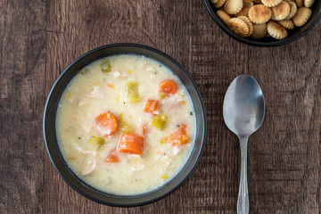 Greek lemon rice soup in a black bowl on a rustic wood table, spoon, oyster crackers