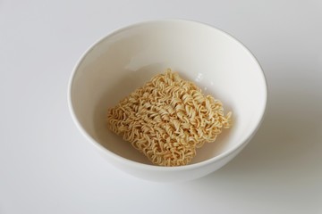 Instant noodles, a dried and precooked noodle block in the white bowl isolated on white background.