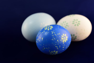Three blue and white painted Easter eggs lie against a blue background with space for text