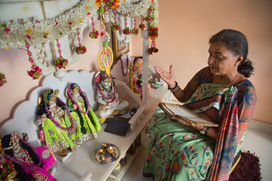 Senior woman reciting prayers during puja at home.	