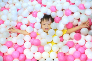 Fototapeta na wymiar Above view portrait of cute little Asian kid in ball pit full of colorful plastic balls smiling at camera while having fun in children play center, indoor playground