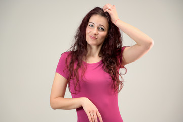 Portrait of a pretty slim brunette woman with emotions in a pink dress and with brown hair on a white background in the studio. The model is smiling and talking nicely.