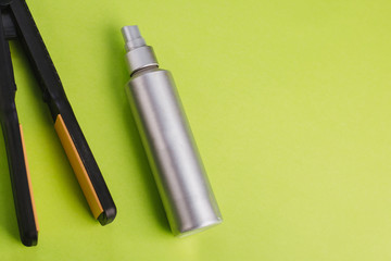 Black Hair Straighteners on a green background and a silver bottle. Barber tool. Hairspray or protective spray