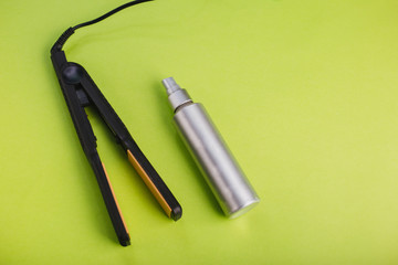 Black Hair Straighteners on a green background and a silver bottle. Barber tool. Hairspray or protective spray