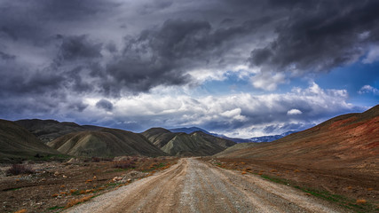 Dirt road to the mountains at stormy weather