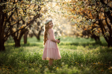 portrait of a cute beautiful girl with blond hair in a pink dress and a wreath of flowers in...