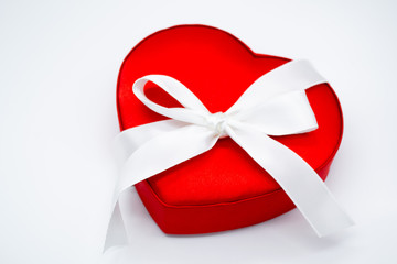 Close up of a bright red satin heart-shaped box with a large white bow on a white background. Concept of love, Valentine's day, gift, beloved, surprise, present, feelings of love. Isolated