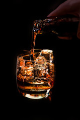 man pours strong alcohol into a glass with ice