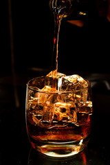strong alcohol whiskey is poured into a glass with ice closeup