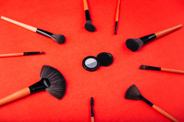 Cosmetics on a bright orange background. Makeup brushes, highlighter and eye shadow with pigments
