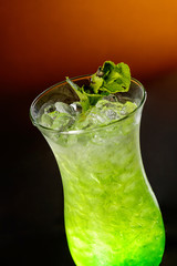 Green cocktail with ice cubes on orange background. Close up