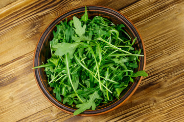 Fresh green arugula in ceramic bowl on a wooden table. Top view. Healthy food or vegetarian concept
