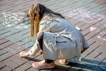 Little girl draws chalk on asphalt