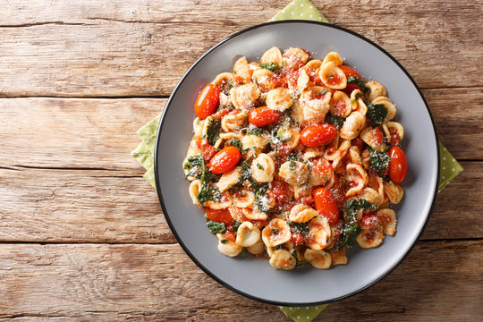 Vegetarian Italian pasta orecchiette with spinach in tomato sauce close-up in a plate. Horizontal top view