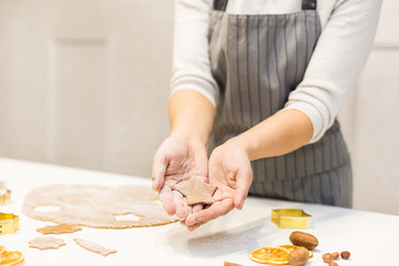 Young pretty woman prepares the dough and bakes gingerbread and cookies in the kitchen. She holds a star cut from the dough in her hands. Merry Christmas and Happy New Year.