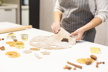 Young pretty woman prepares the dough and bakes gingerbread and cookies in the kitchen. She makes a star shape on the dough. Merry Christmas and Happy New Year.