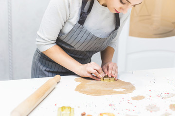 Young pretty woman prepares the dough and bakes gingerbread and cookies in the kitchen. She makes a star shape on the dough. Merry Christmas and Happy New Year.