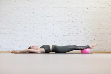 Foto op Canvas Full body stretching and relax. Beautiful caucasian woman lying on the floor with feet on small fit ball and hands up in loft fitness studio indoor, selective focus. © junky_jess