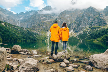 man with woman in yellow raincoat at sunny autumn day looking at lake in tatra mountains - obrazy, fototapety, plakaty