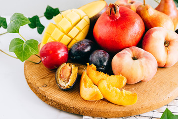 Assorted fruits in a wooden board on a marble background, green ivy mango, peach, plum, pear, pomegranate, fig peach