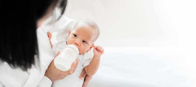 Mother feeding asian baby with bottle of milk, banner copy space