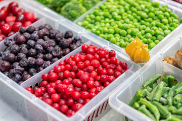 Frozen fruits and vegetables. Products are poured into plastic boxes. In the center of the frame is red and black currants. Freezer shop window.