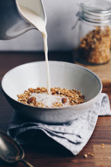 Almond milk is poured in a ceramic bowl with baked granola. Healthy vegetarian breakfast.