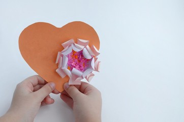 A heart made of orange paper with a flower, the child holds in his hands. With free space for text.