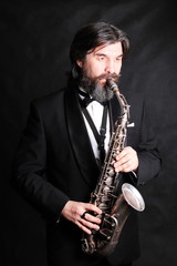 Fototapeta na wymiar A male artist musician in a classic black suit, tailcoat, statuesque in a bow tie with a beard plays music on a gold saxophone.black background