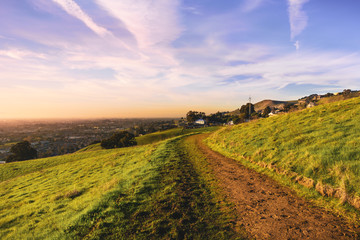 Sunset view of hiking trail on the verdant hills of East San Francisco Bay Area; the City of Hayward visible in the background; California